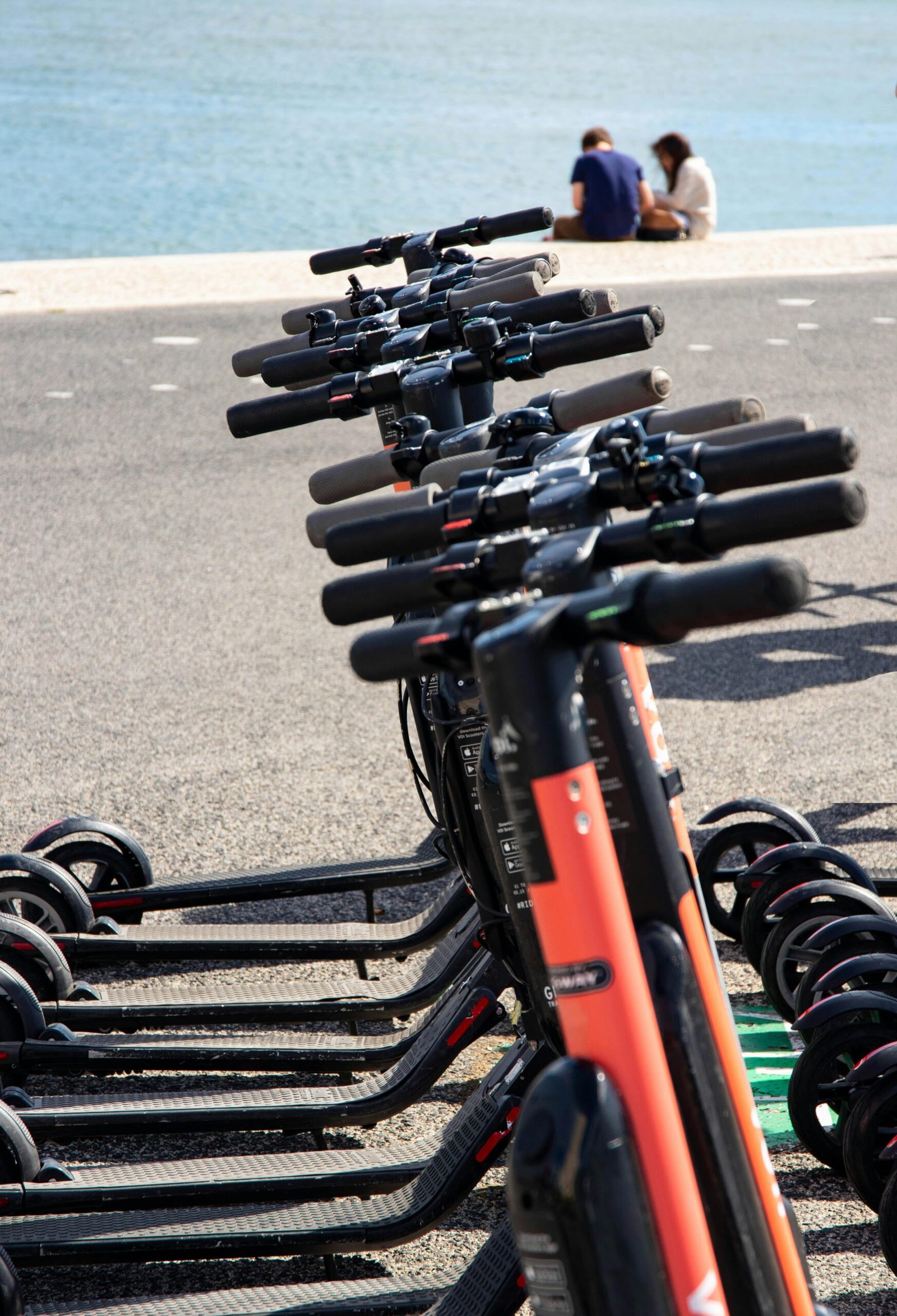  electric scooters parked side by side on a city sidewalk, with a modern urban backdrop and clear skies.